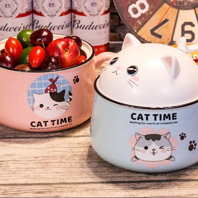 Cat-themed ceramic kawaii ramen bowl and mug on a wooden surface with colorful cherries and a clock in the background.
