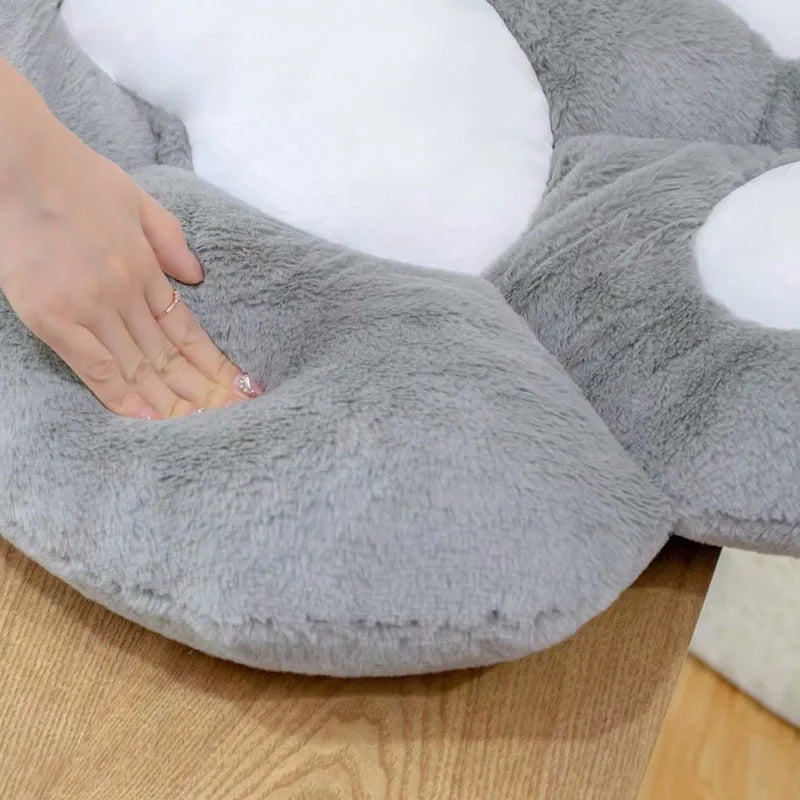 Gray kawaii pillow with a hand resting on it, on a wooden floor.
