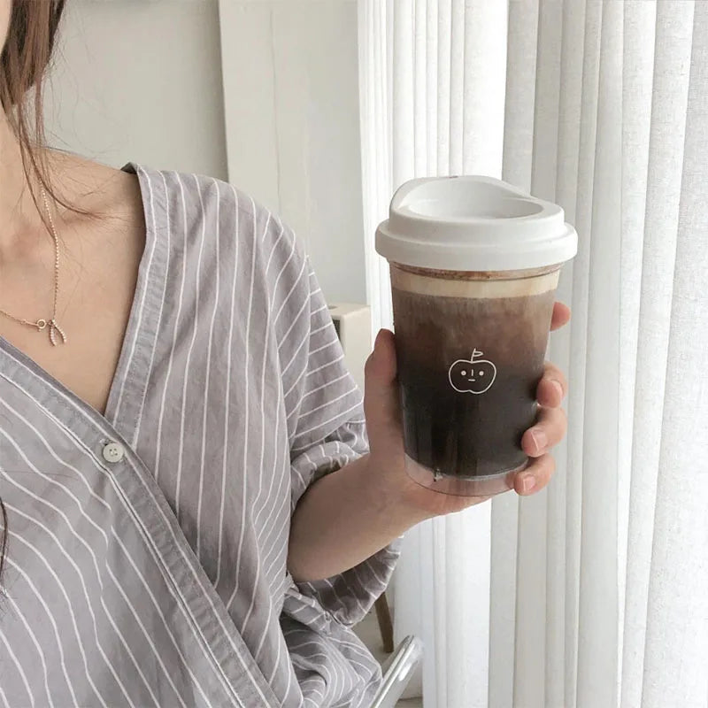 Person holding a coffee Kawaii cup with a white lid indoors