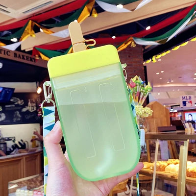 Hand holding a green popsicle-shaped kawaii water bottle with a colorful background