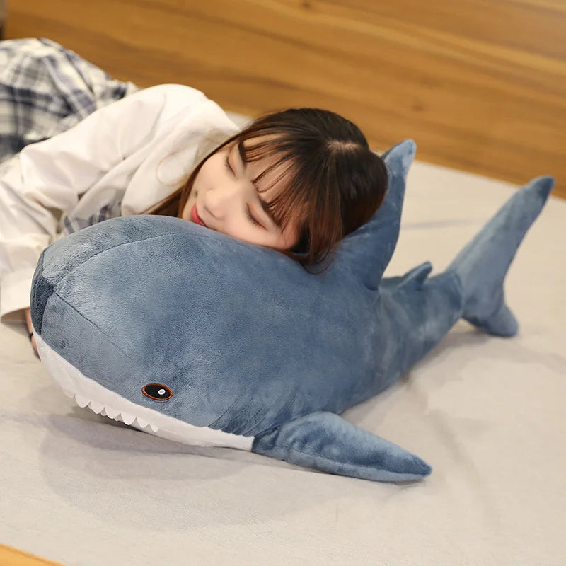 Child lying on a bed with a large blue shark-shaped kawaii pillow