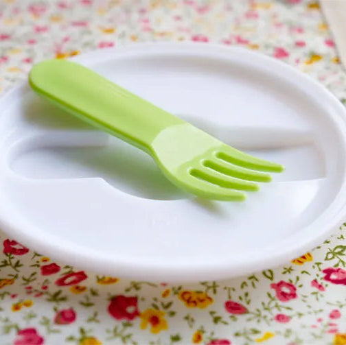 White plate with a green kawaii fork on a floral tablecloth