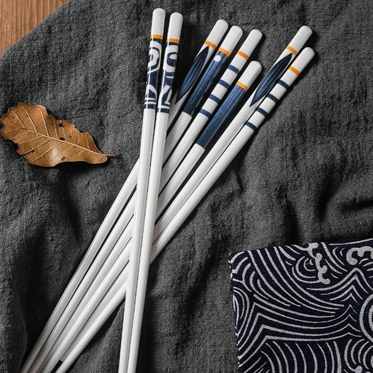 Set of white kawaii chopsticks with blue and orange accents on a dark fabric background.