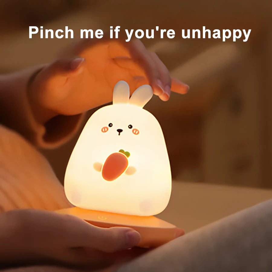 Cute kawaii rabbit-shaped night light with a carrot design, held by a hand with text 'Pinch me if you're unhappy'.