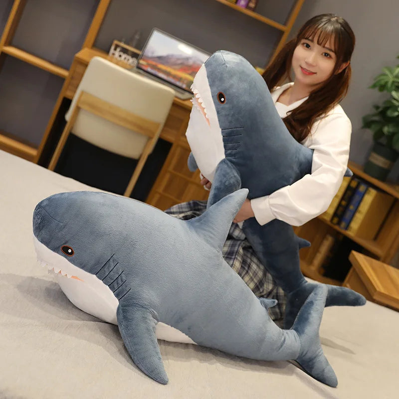 Person holding a large shark-shaped kawaii plush toy in a room with a desk and books.