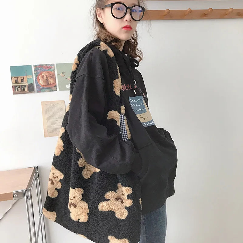 Person wearing a black jacket with kawaii teddy bear pattern and a tote bag in a room.