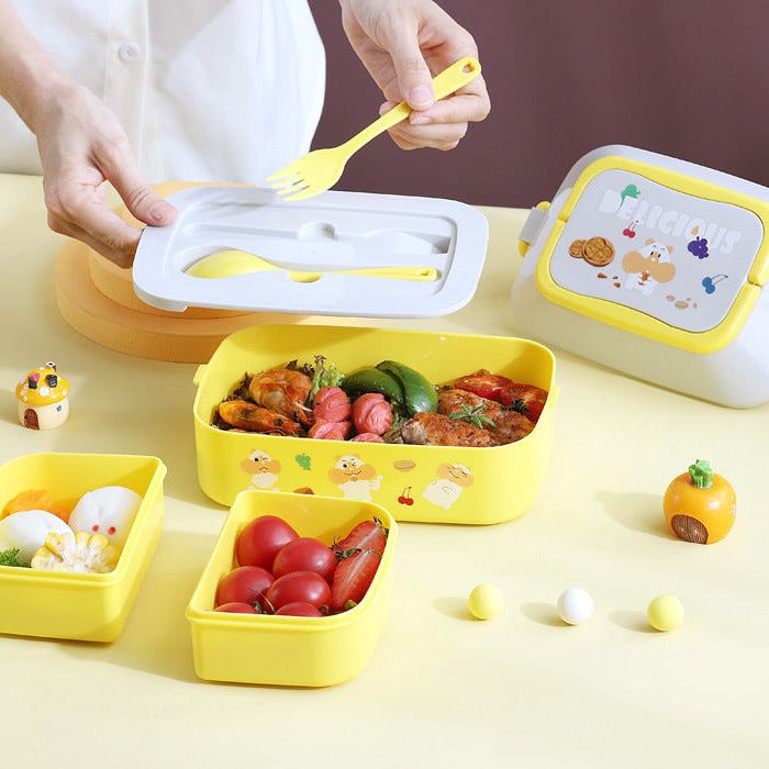 Yellow kawaii lunch box with utensils and food on a yellow surface, with a person using the spoon.
