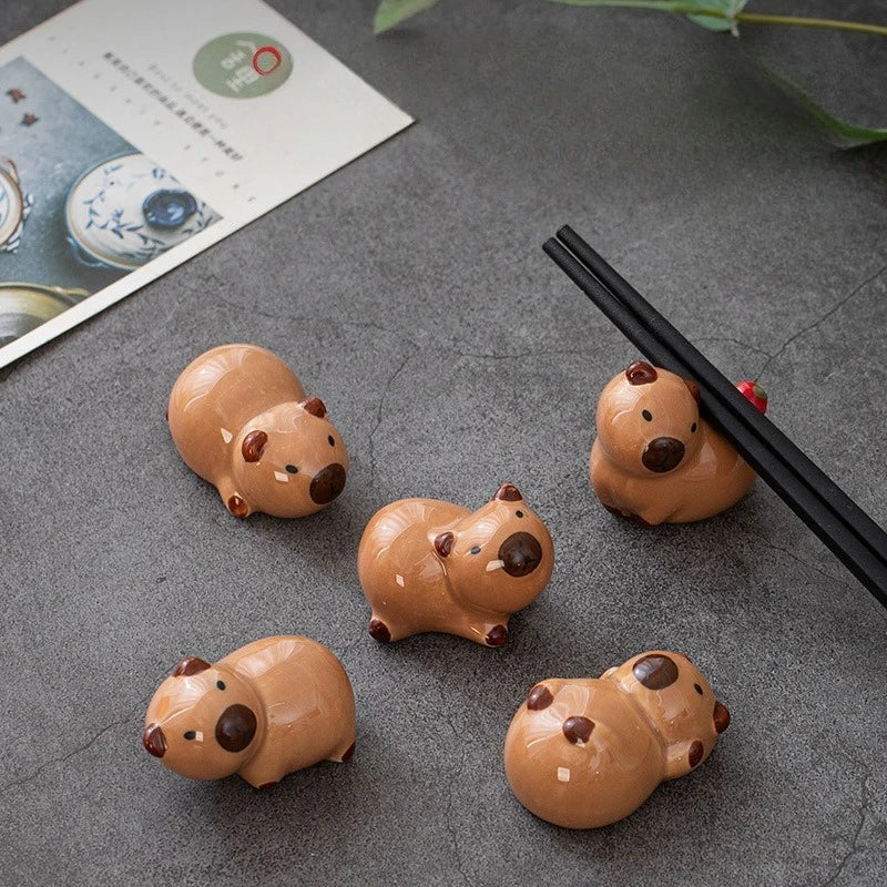 Five small brown ceramic kawaii animals on a gray surface with black chopsticks.