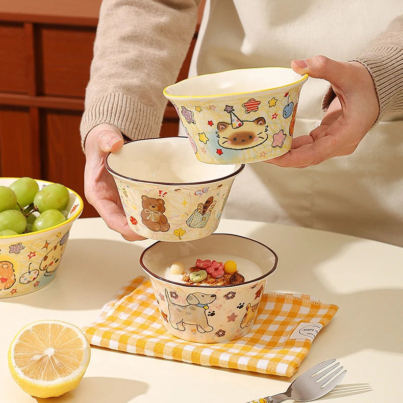 Person holding a set of ceramic kawaii ramen bowls with animal patterns on a table.
