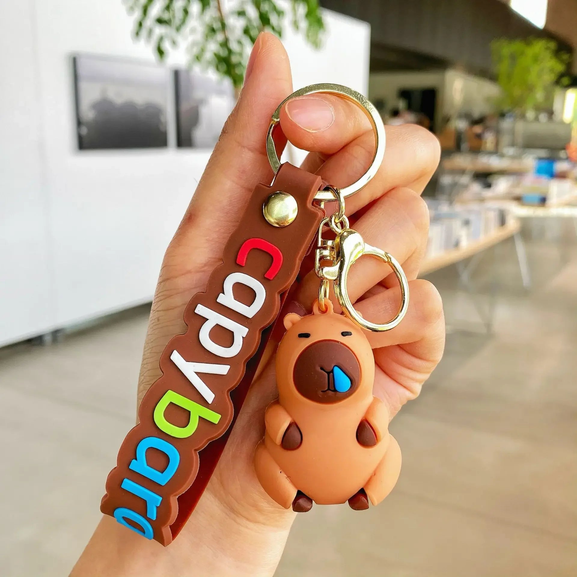 Hand holding a kawaii keychain with a bear charm and colorful text in an indoor setting