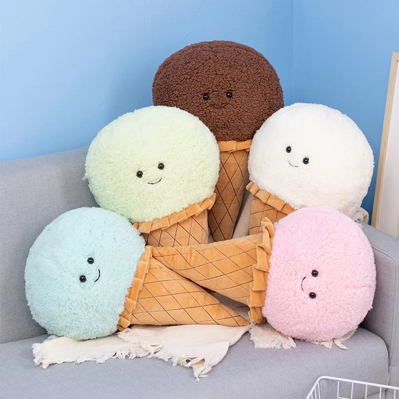 Five colorful kawaii plush ice cream cones with faces on a gray couch against a blue wall.