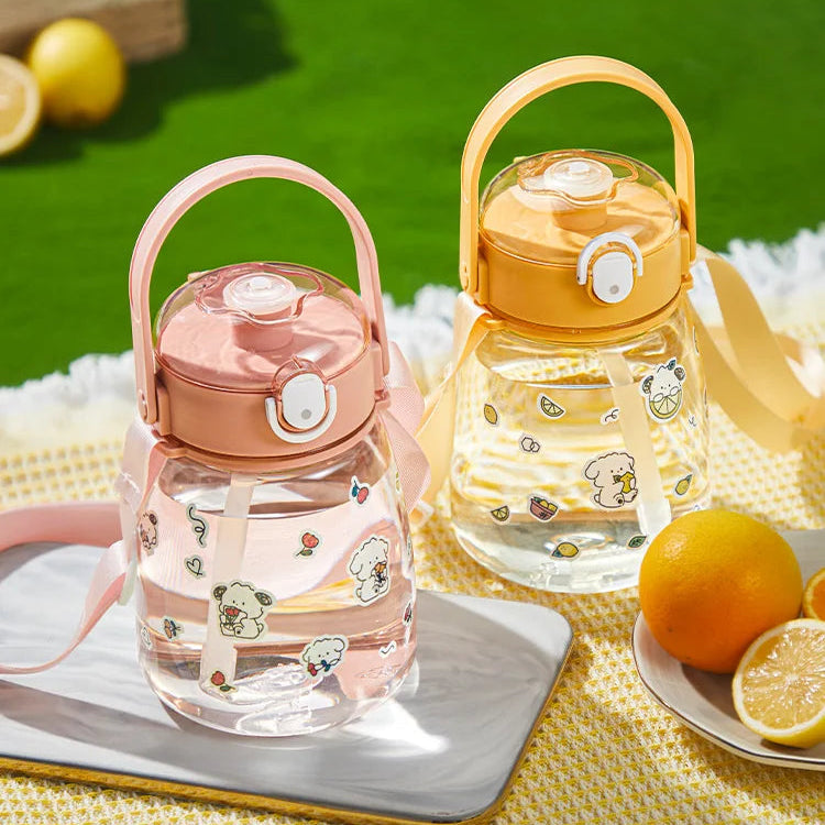 Two colorful kawaii water bottles with handles on a green outdoor surface with lemons.