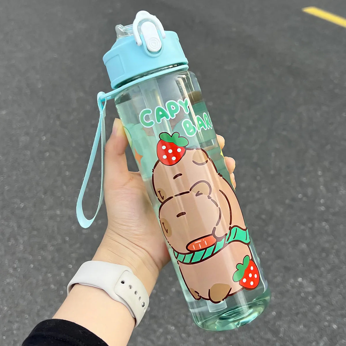 Clear kawaii water bottle with cartoon design and blue cap held by a hand on a dark surface