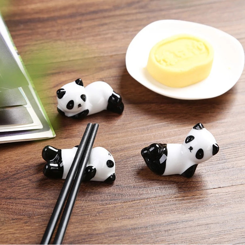 Panda-shaped kawaii chopstick holders on a wooden surface with a plate of food in the background.