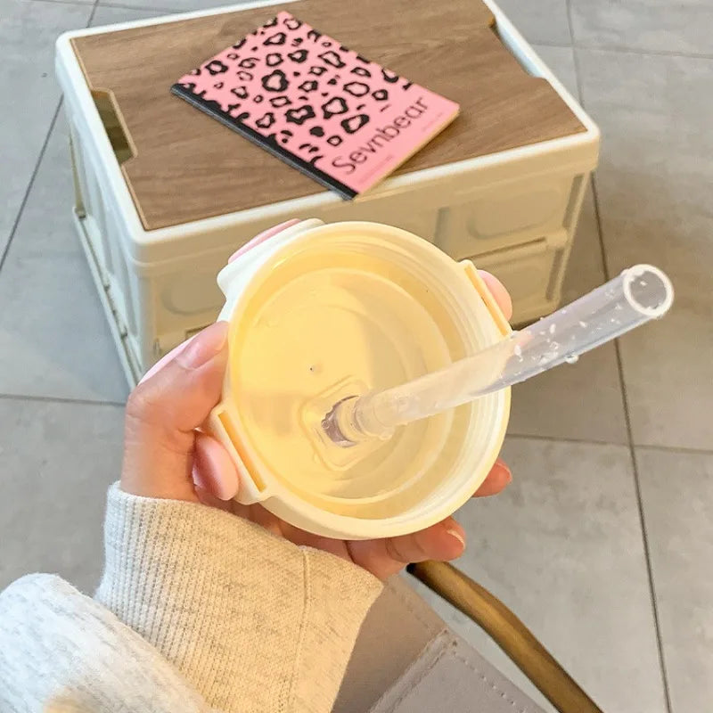 Hand holding a yellow kawaii cup with a straw, pink leopard print napkin in the background
