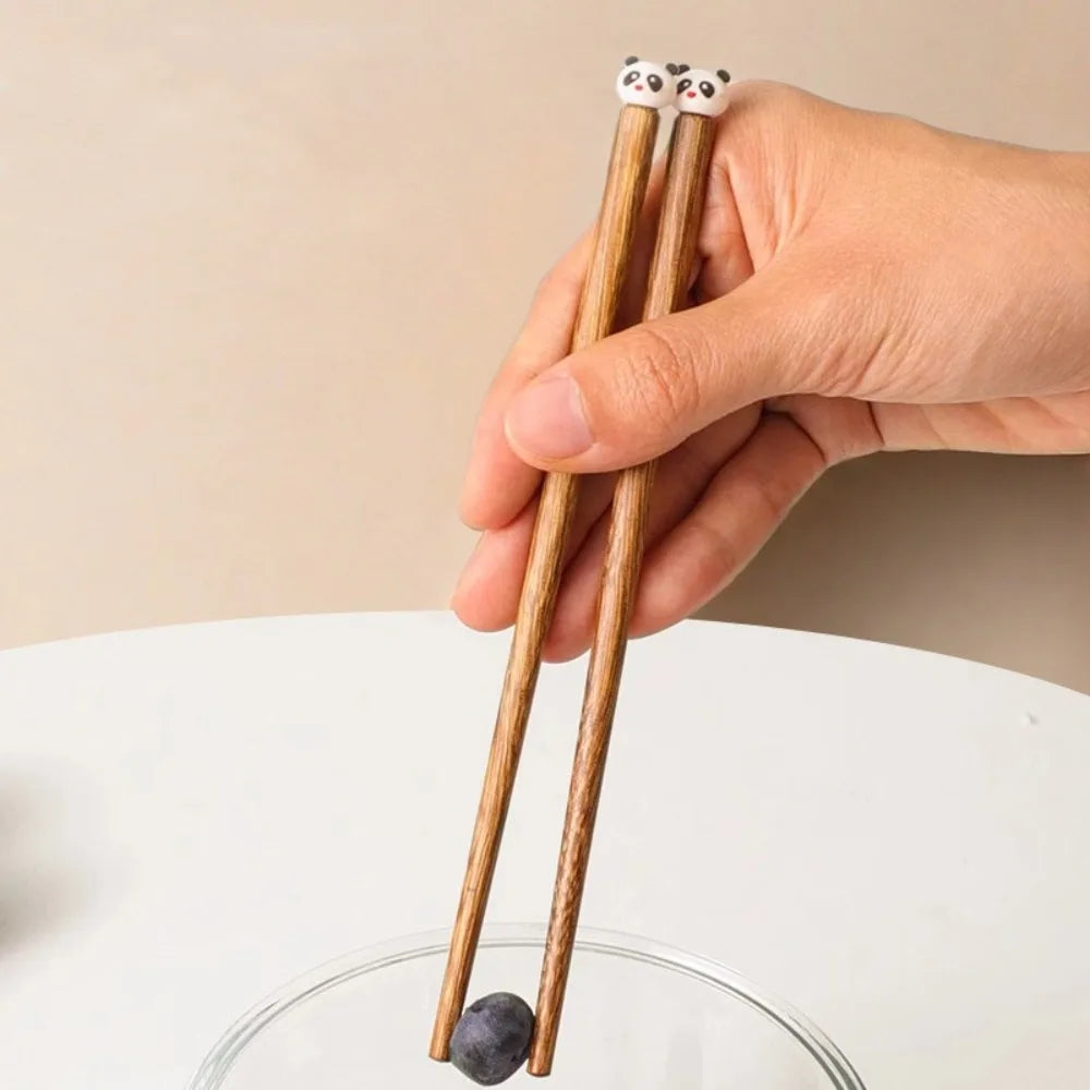 Hand holding a pair of wooden kawaii chopsticks with panda ends on a neutral background