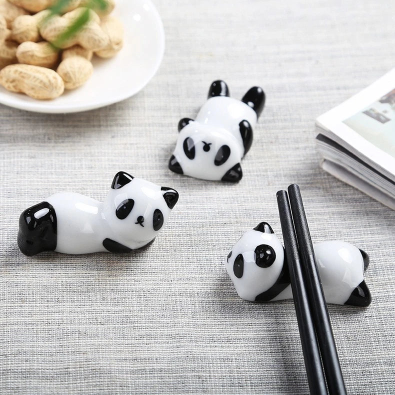 Three panda-shaped kawaii chopstick holders on a table with peanuts and a book in the background.