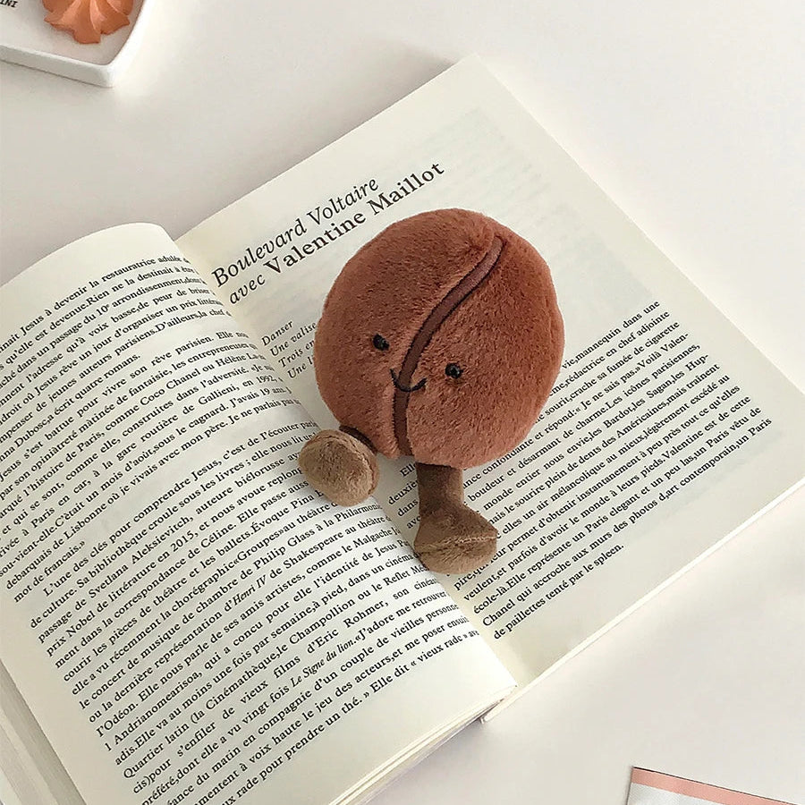 Kawaii plush toy resembling a chocolate cookie on an open book with a light background