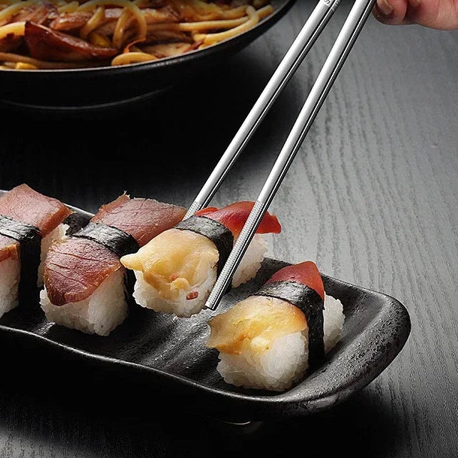 Hand using kawaii chopsticks to pick up sushi from a black plate with a blurred background of French fries.