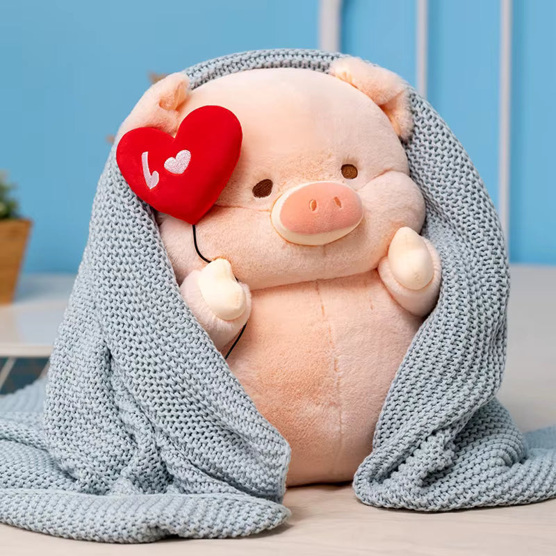 A cute pink plush pig toy wrapped in a light blue-gray knitted blanket, holding a red heart-shaped balloon with a white heart on it.