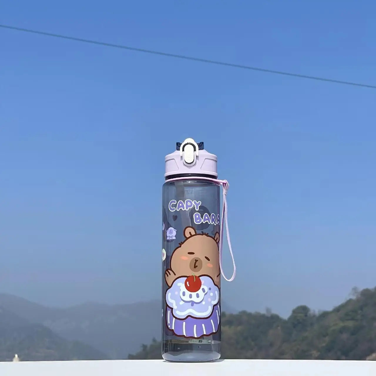 Capybara-themed kawaii water bottle with a bear design against a blue sky and mountain background