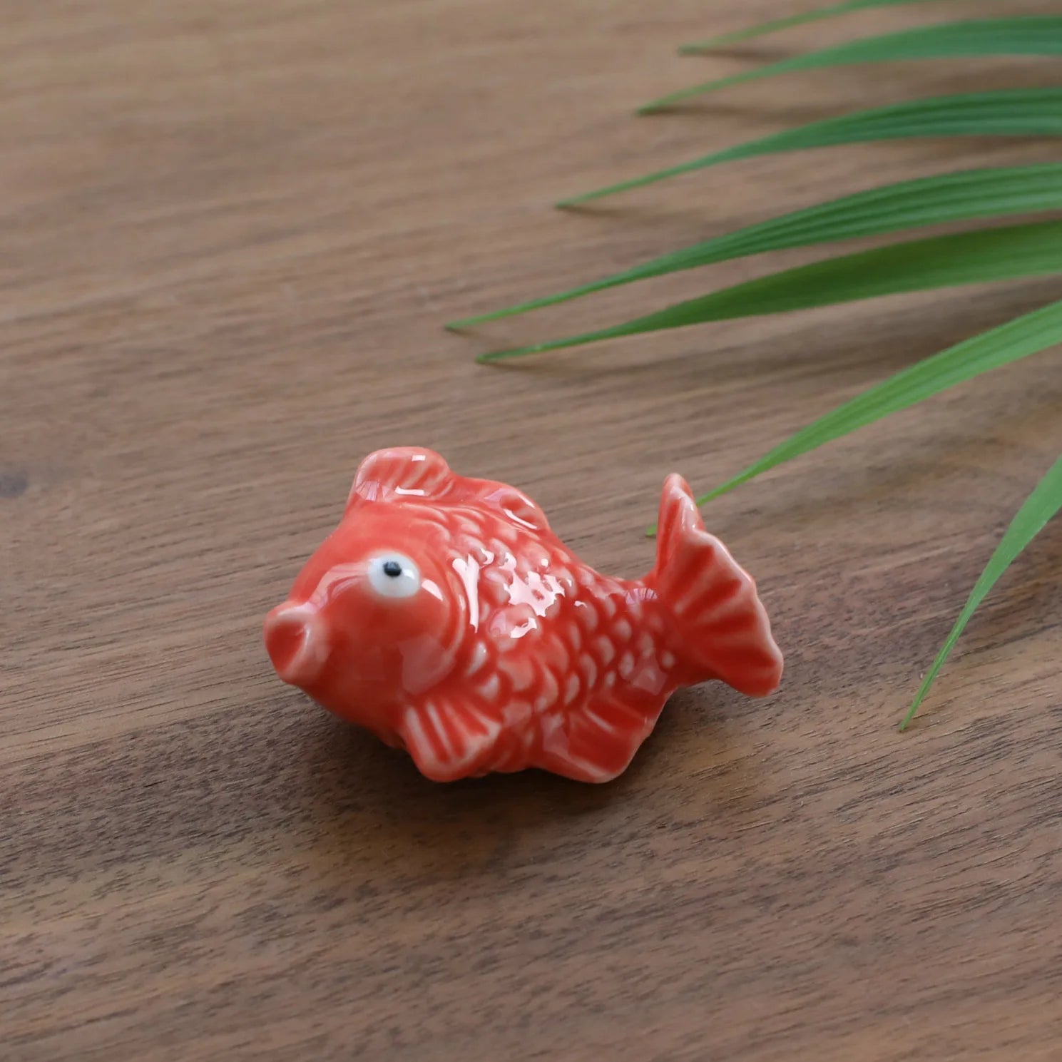 Small red ceramic fish kawaii chopstick holders on a wooden surface with green leaves.