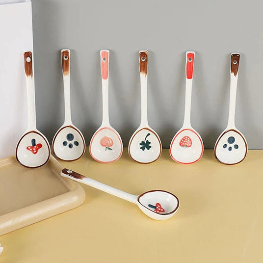 Set of ceramic kawaii spoons with decorative handles on a beige surface.