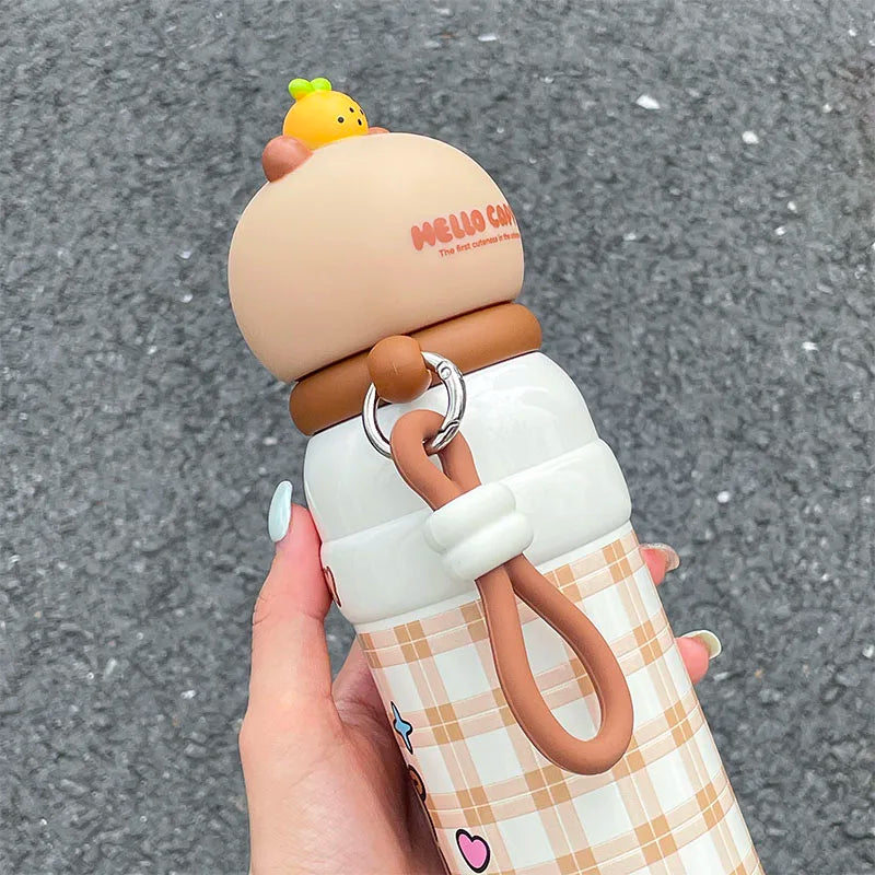 Hand holding a cute kawaii water bottle with a cartoon character on a gray pavement background