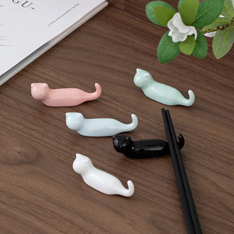 Cat-shaped ceramic kawaii chopstick holders on a wooden surface with a plant and book in the background.