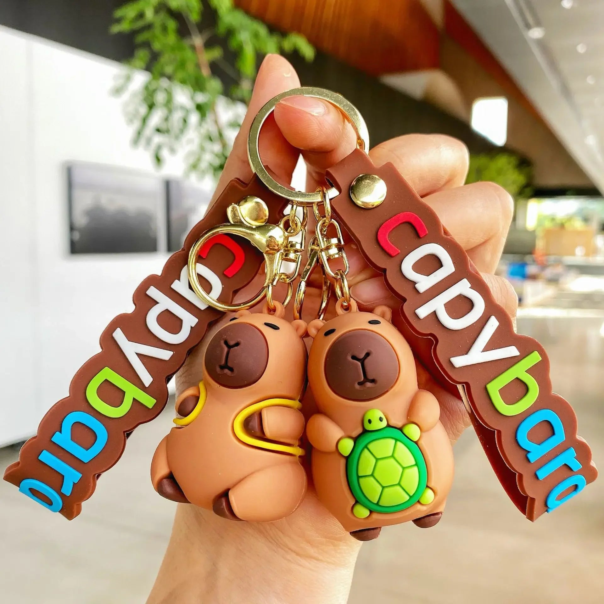 Capybara-shaped kawaii keychain with a person holding it in a blurred indoor background