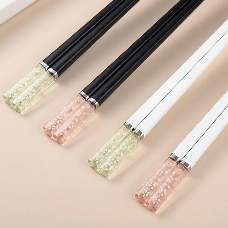 Four pairs of decorative kawaii chopsticks with black, white, and pink handles on a beige background