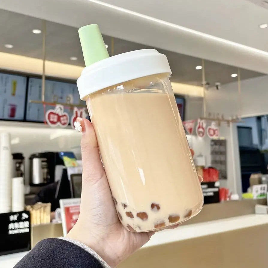 Hand holding a kawaii water bottle of bubble tea with a straw in a cafe setting