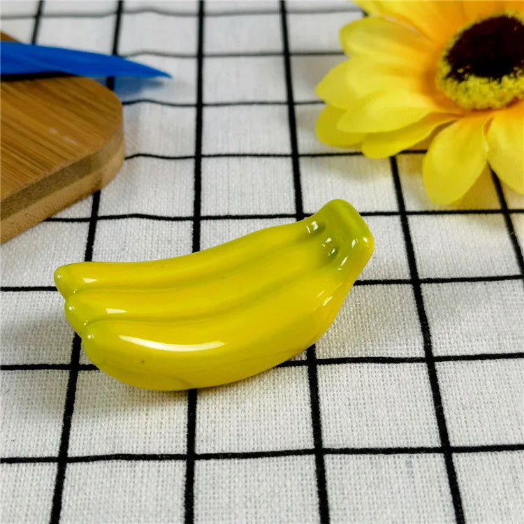 Yellow ceramic banana kawaii chopstick holders on a grid-patterned surface with a sunflower and wooden coaster in the background.