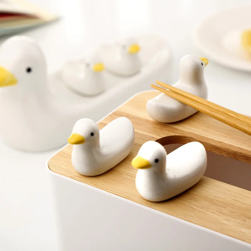 White ceramic duck-shaped kawaii chopstick holders on a wooden board with a white background