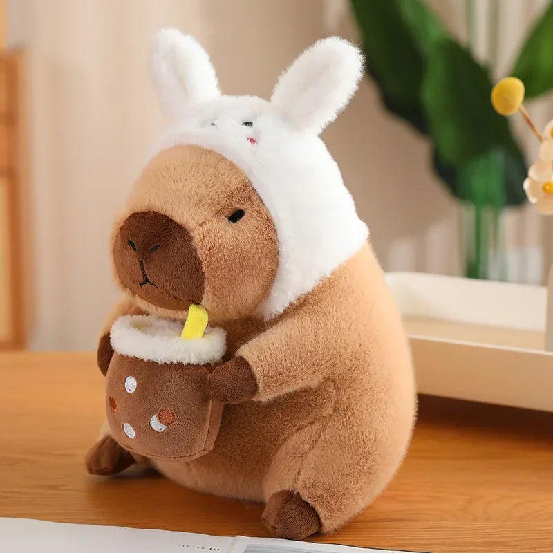 Kawaii plush toy resembling a bear in a bunny costume holding a hot chocolate mug on a wooden surface.