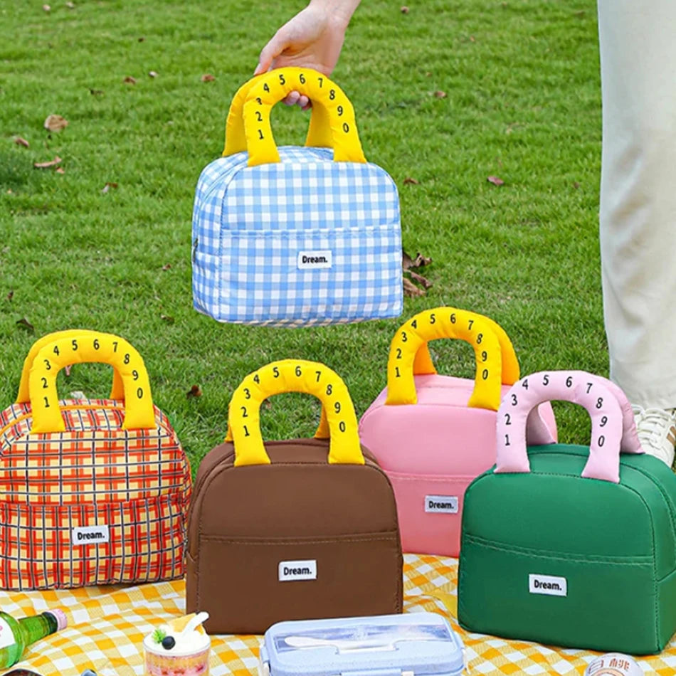 Colorful insulated kawaii lunch bags with cartoon character handles on a grassy background