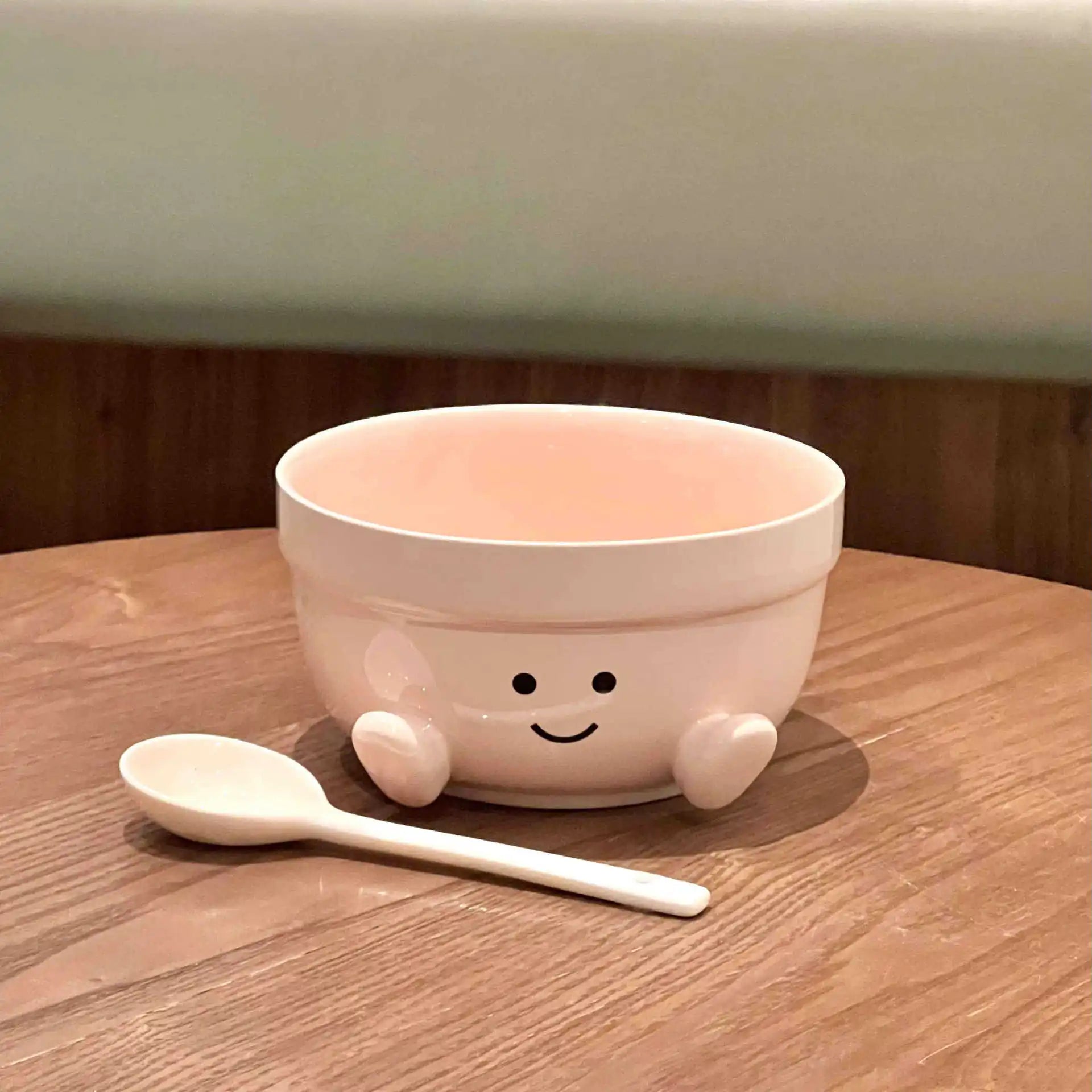 Cute ceramic kawaii bowl with a smiling face design on a wooden surface with a spoon next to it.
