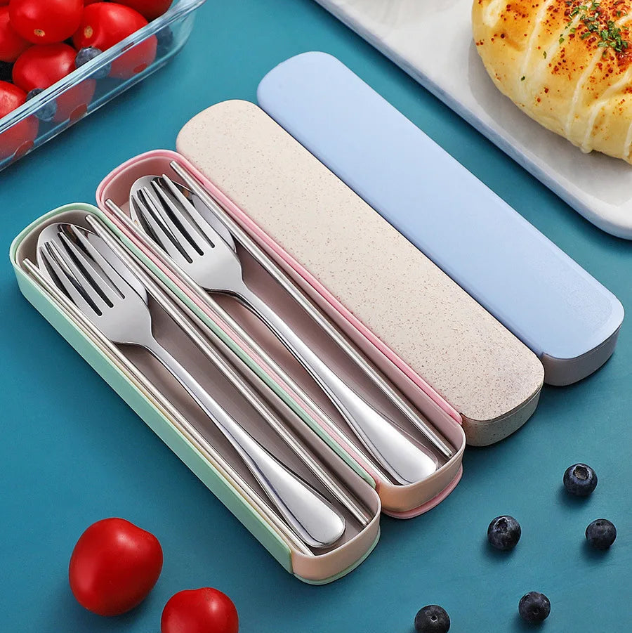 Set of silver kawaii utensils in a pink case on a blue background with tomatoes and bread.