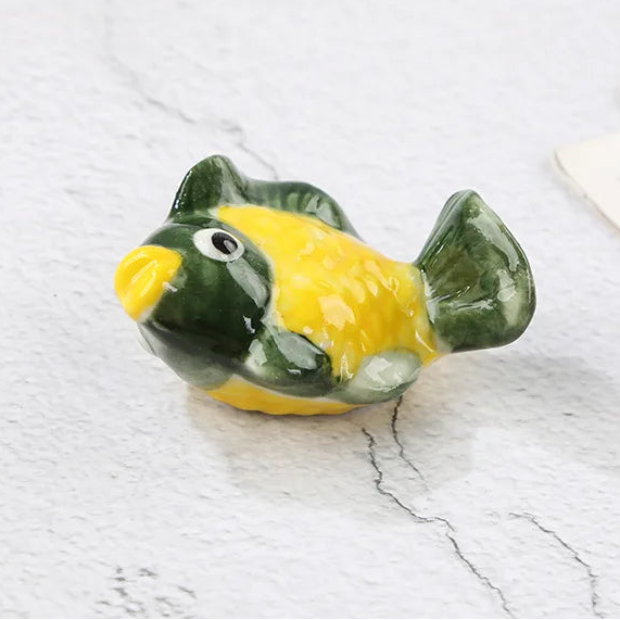 Small green and yellow ceramic fish kawaii chopstick holders on a marble surface with text indicating dimensions.