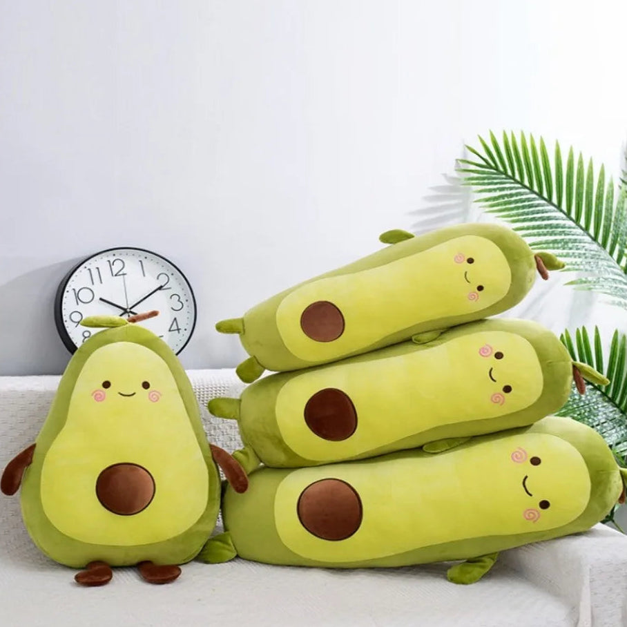 Stack of avocado-shaped kawaii plush toys on a white surface with a clock and plant in the background.
