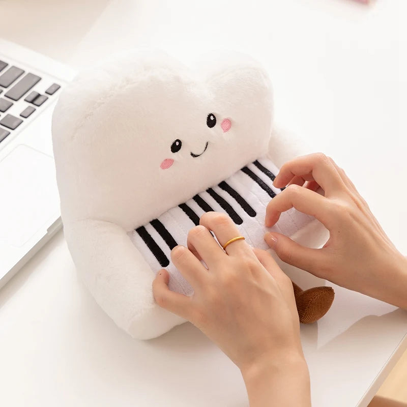 Kawaii plush piano toy with a face being played on by hands on a desk.