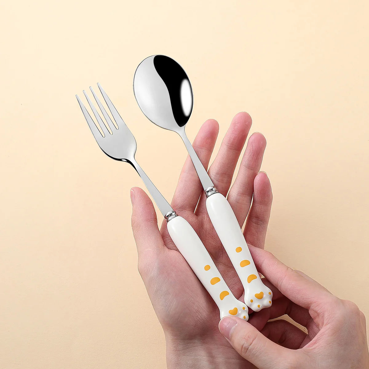 Hand holding kawaii utensils with white handles featuring small yellow patterns on a beige background