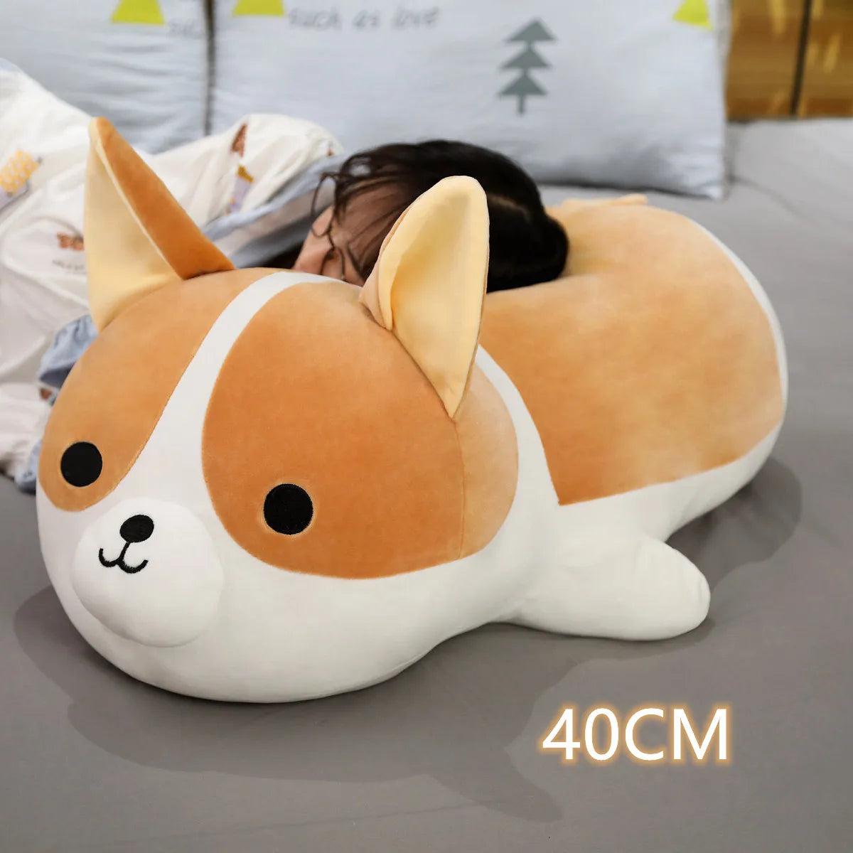 Corgi-shaped kawaii pillow on a bed with a person lying behind it, size indicated as 40CM.