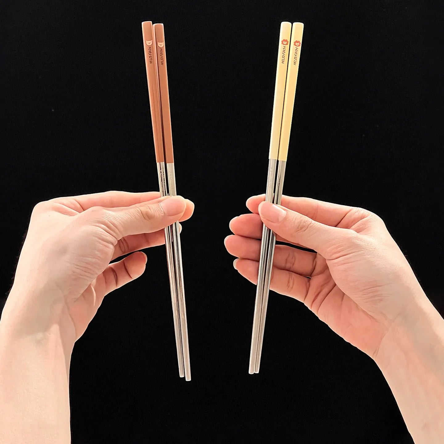 Two pairs of kawaii chopsticks held by hands against a black background
