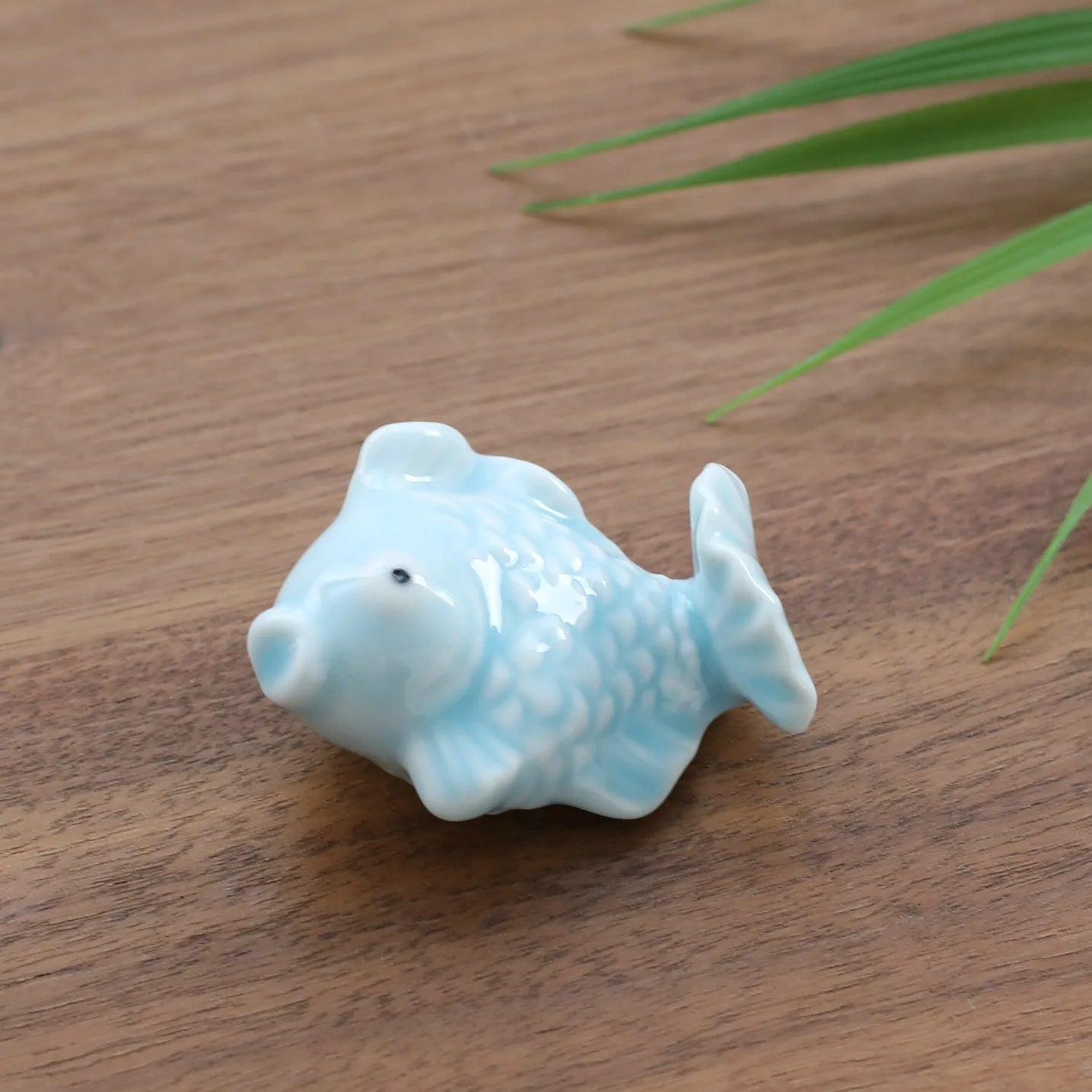 Ceramic fish kawaii chopstick holders on a wooden surface with green leaves