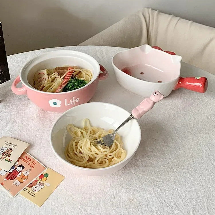 Two kawaii ramen bowls of noodles with a pink and white bowl on a light-colored surface.