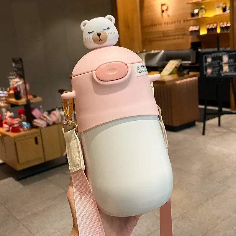 Pink and white insulated kawaii mug with bear lid held in a hand, blurred indoor background