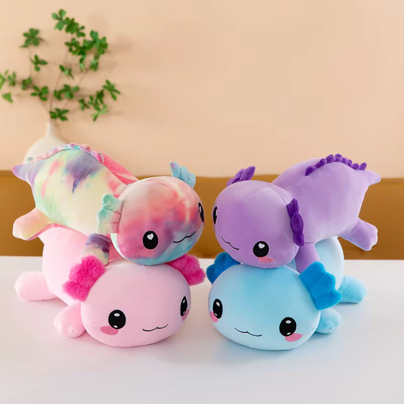 Four pastel axolotl plush toys arranged together on a white surface against a warm beige wall, with a small green plant in the background.