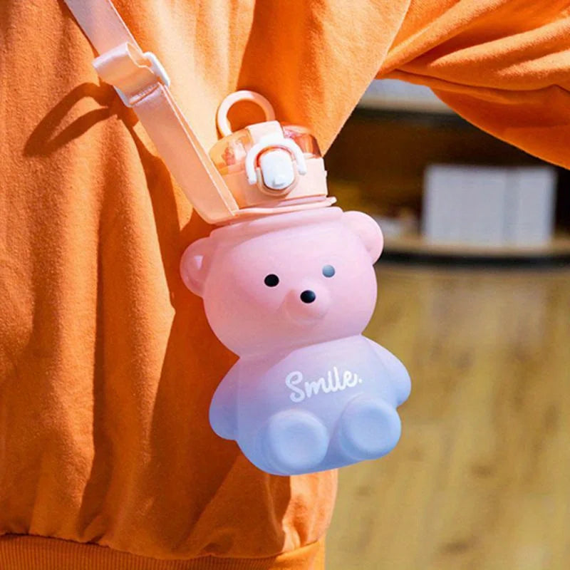 Pink bear-shaped kawaii water bottle with a cloud design and 'Smile' text, attached to an orange shirt.