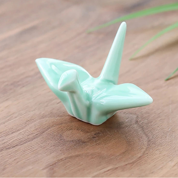 Green ceramic kawaii chopstick holders on a wooden surface with grass in the background